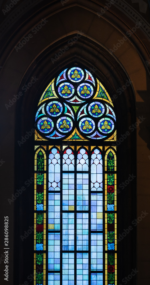 A high stained glass window with colored accents in an old Catholic church.