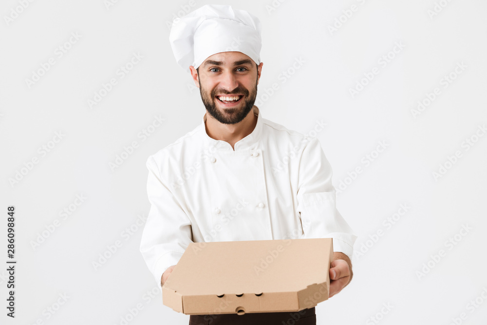 Image of joyful baker man in cook uniform smiling and holding pizza box Image of joyful baker man in cook uniform smiling and holding pizza box