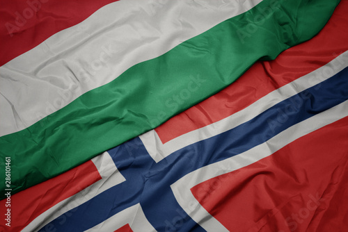 waving colorful flag of norway and national flag of hungary.