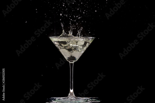 glass of martini and splash from falling ice on a black background