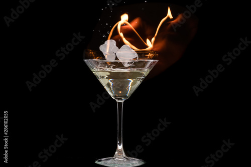 glass of martini with olives and ice on a black background and fire