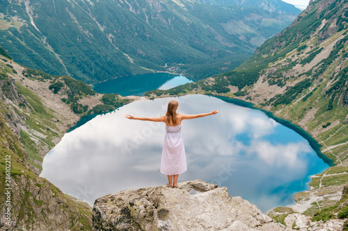Beautiful long haired girl in white dress standing with hands apart in Polish mountains with fabulous scenic view on background