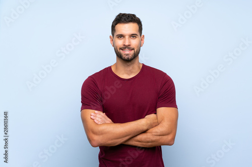 Handsome man over isolated blue background keeping the arms crossed in frontal position