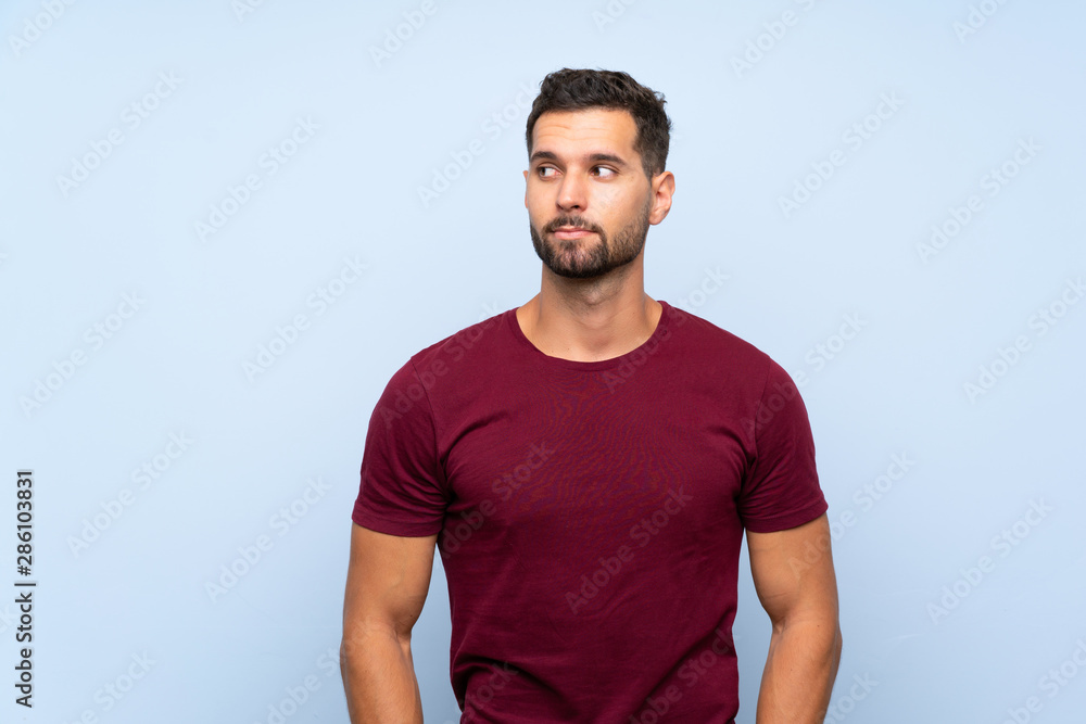 Handsome man over isolated blue background making doubts gesture looking side Handsome man over isolated blue background making doubts gesture looking side