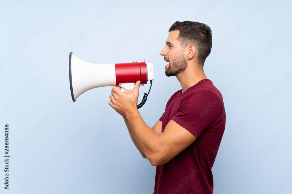 Handsome man over isolated blue background shouting through a megaphone Handsome man over isolated blue background shouting through a megaphone
