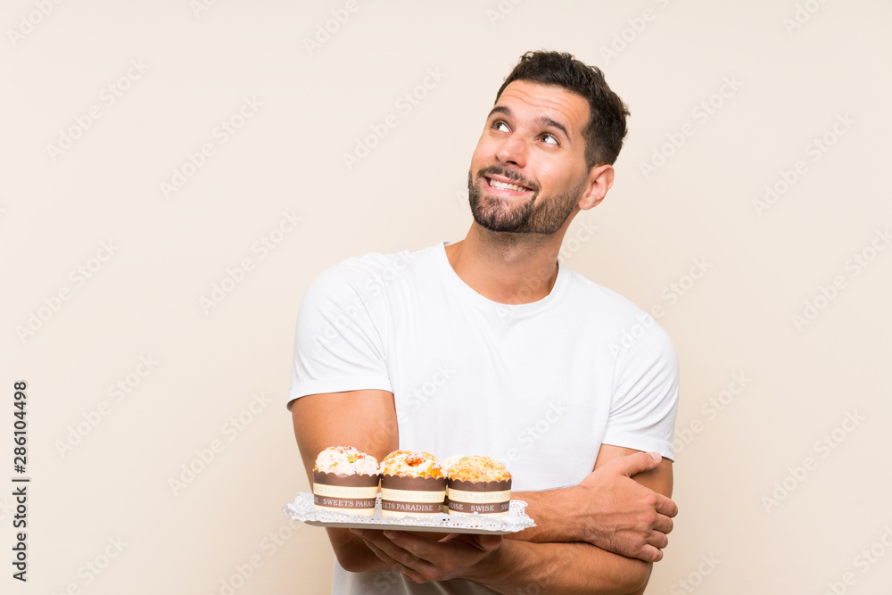 Handsome man holding muffin cake over isolated background looking up while smiling Handsome man holding muffin cake over isolated background looking up while smiling