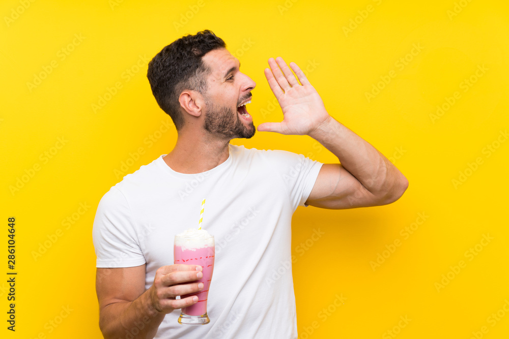 Young man with strawberry milkshake over isolated yellow background shouting with mouth wide open Young man with strawberry milkshake over isolated yellow background shouting with mouth wide open