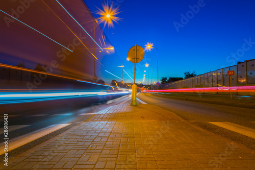 Rozmyty tir ruch drogowy rozmazane światła, na środku znak drogowy i swiecące latarnie
