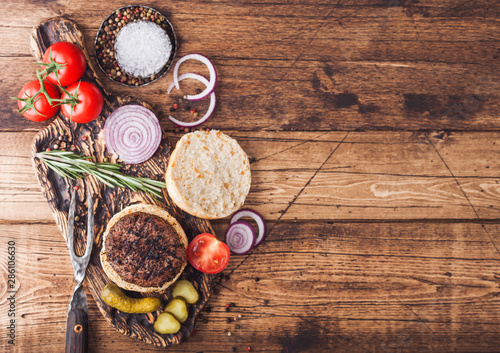 Fresh grilled minced pepper beef burger on vintage chopping board with buns onion and tomatoes on wooden background. Top view . Space for text