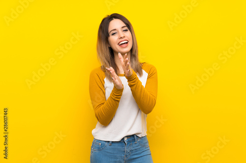 Pretty young woman over isolated yellow wall applauding after presentation in a conference