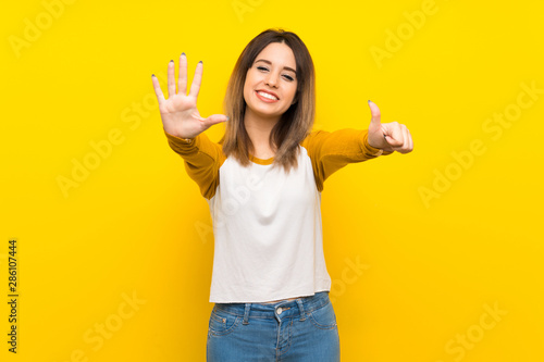 Pretty young woman over isolated yellow wall counting six with fingers