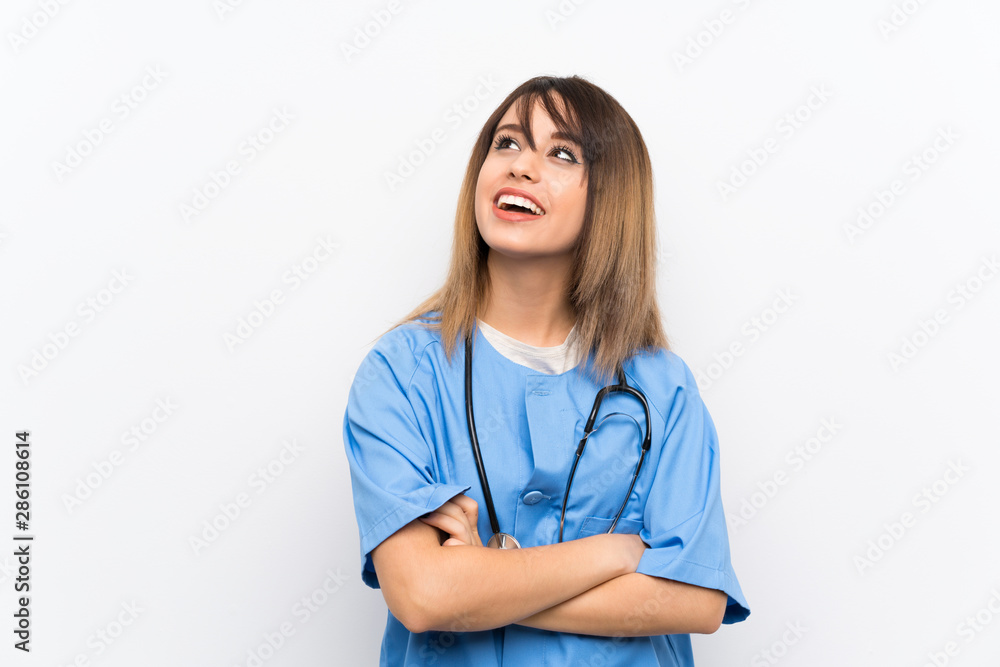 Young nurse woman over white wall looking up while smiling Young nurse woman over white wall looking up while smiling