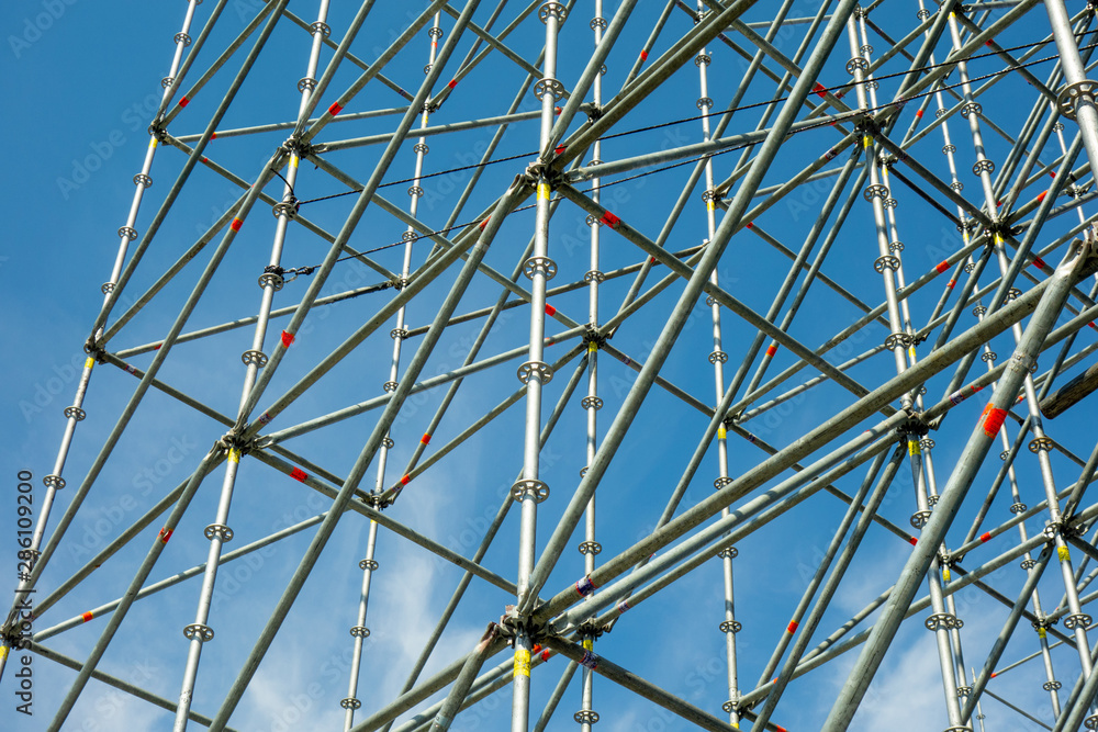 Naklejka premium Metal pipe frame structure on blue sky background. Industrial construction from tubes raises upwards. Building process and joining elements view. Straight and inclined lines backdrop