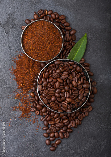 Fresh raw organic coffee beans with ground powder and coffee trea leaf on black background.