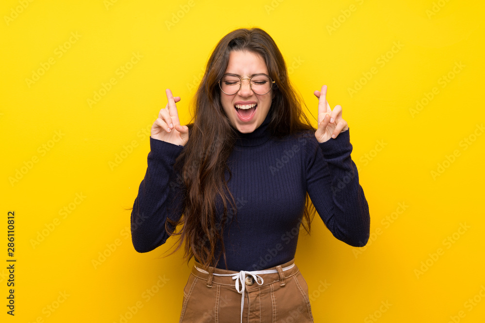Teenager girl over isolated yellow wall with fingers crossing Teenager girl over isolated yellow wall with fingers crossing
