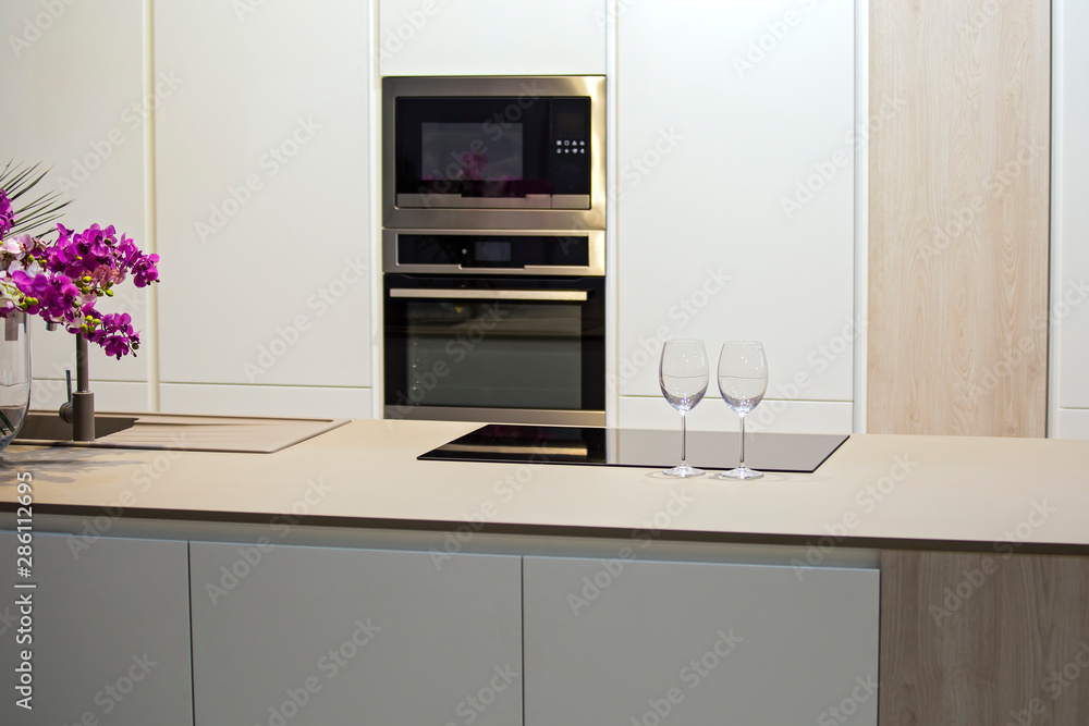 Obraz Minimalistic kitchen design with island. Gray-white kitchen and wine glasses on the table