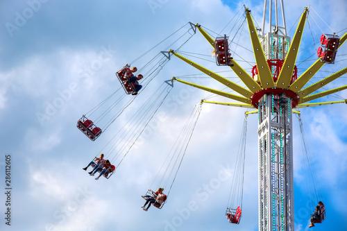 Flying swing carousel in action against cloudy sky. People enjoy a ride on a flying swing ride at an amusement park.