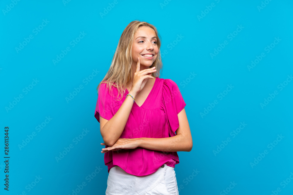 Blonde young woman over isolated blue background thinking an idea while looking up Blonde young woman over isolated blue background thinking an idea while looking up
