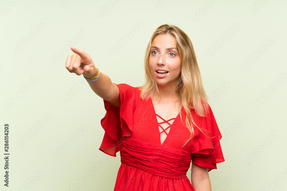 Blonde young woman over isolated green background pointing away Blonde young woman over isolated green background pointing away