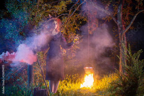 young witch by fire in night forest