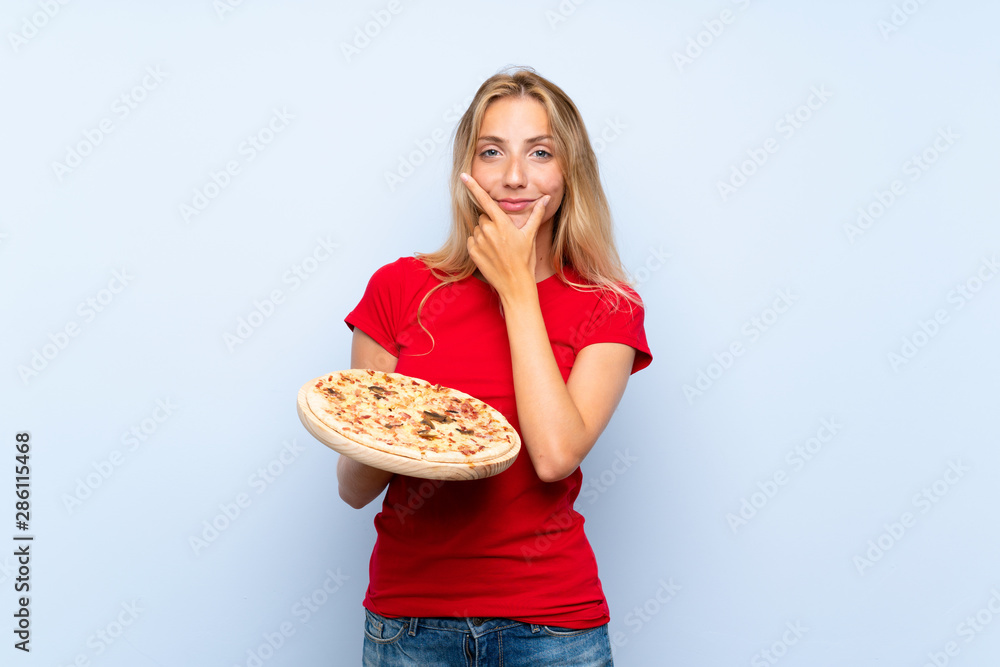 Young blonde woman holding a pizza over isolated blue wall thinking an idea Young blonde woman holding a pizza over isolated blue wall thinking an idea