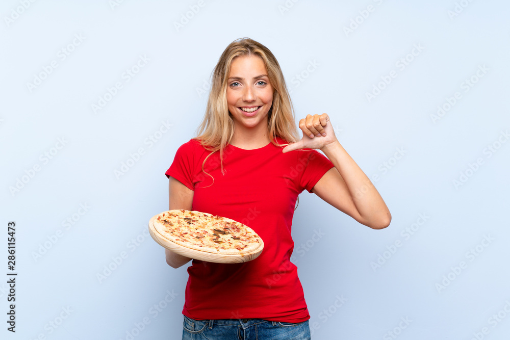 Young blonde woman holding a pizza over isolated blue wall proud and self-satisfied Young blonde woman holding a pizza over isolated blue wall proud and self-satisfied