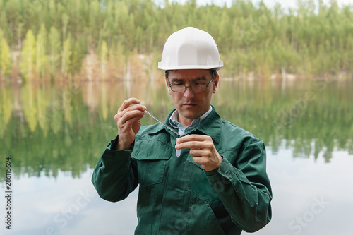 industrial ecologist takes a sample of water from lake at the site of a flooded quarry photo