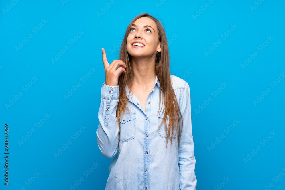 Young woman over isolated blue background pointing up and surprised Young woman over isolated blue background pointing up and surprised