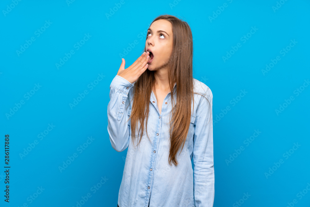 Young woman over isolated blue background yawning and covering wide open mouth with hand Young woman over isolated blue background yawning and covering wide open mouth with hand