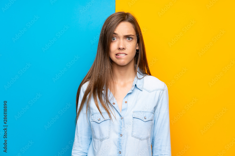 Young woman over colorful background having doubts and with confuse face expression