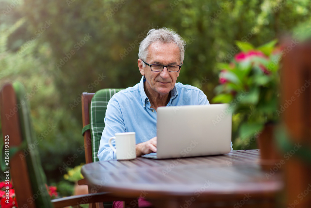Senior man working on laptop in the garden - obrazy, fototapety, plakaty 