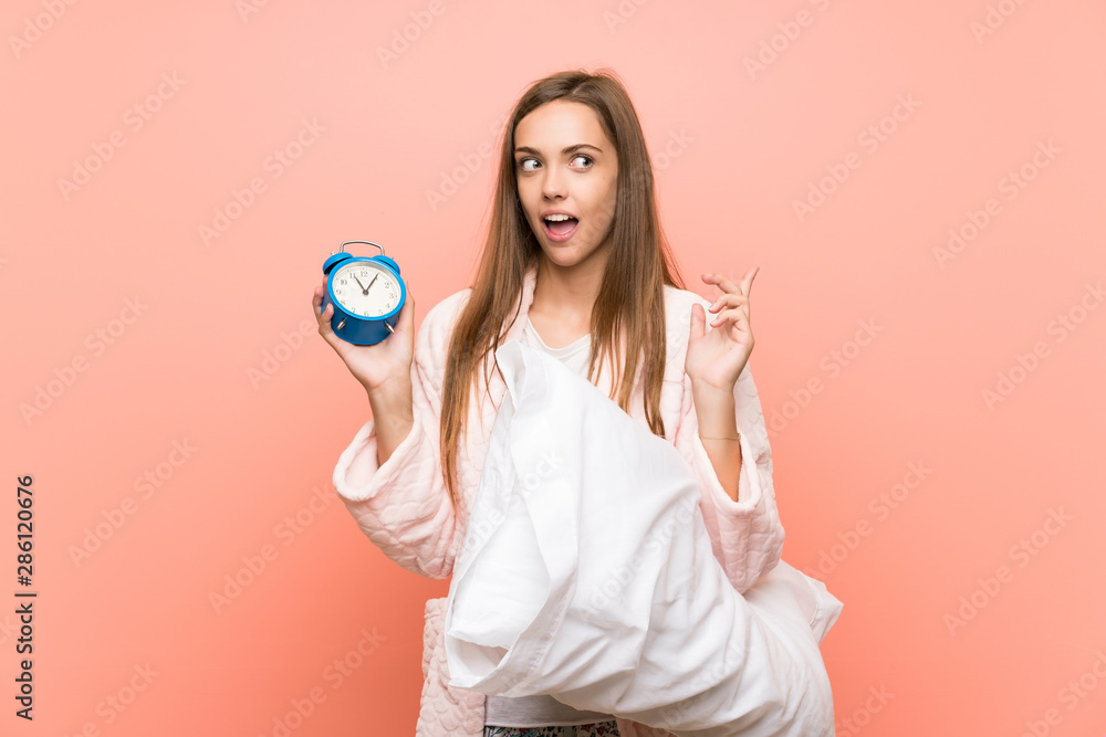 Young woman in dressing gown over pink wall holding vintage clock Young woman in dressing gown over pink wall holding vintage clock
