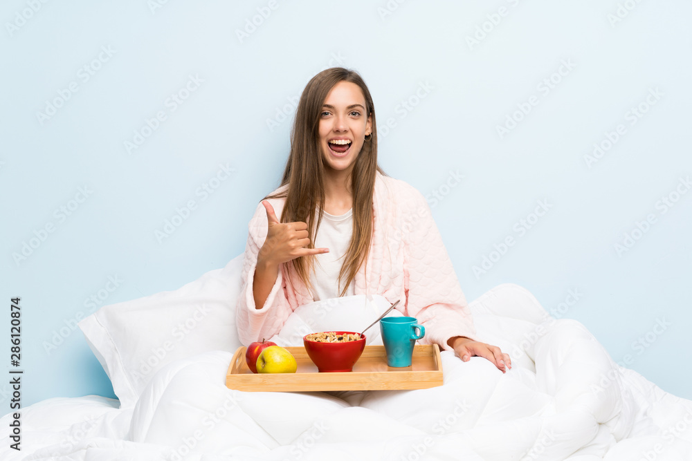 Young woman in dressing gown with breakfast making phone gesture Young woman in dressing gown with breakfast making phone gesture