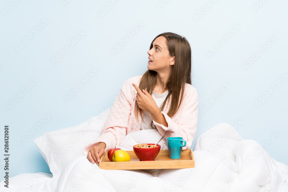 Young woman in dressing gown with breakfast pointing back with the index finger Young woman in dressing gown with breakfast pointing back with the index finger