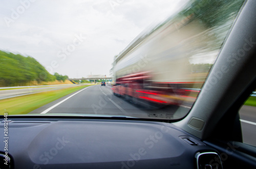 Car is going to overtake white / red truck on European two-lane highway at high speed. Dashboard view with motion blur.
