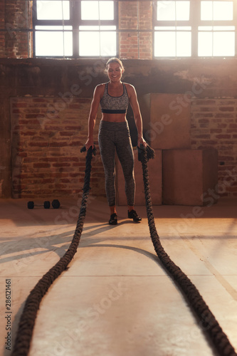 Fitness workout. Sport woman doing battle rope exercise at gym