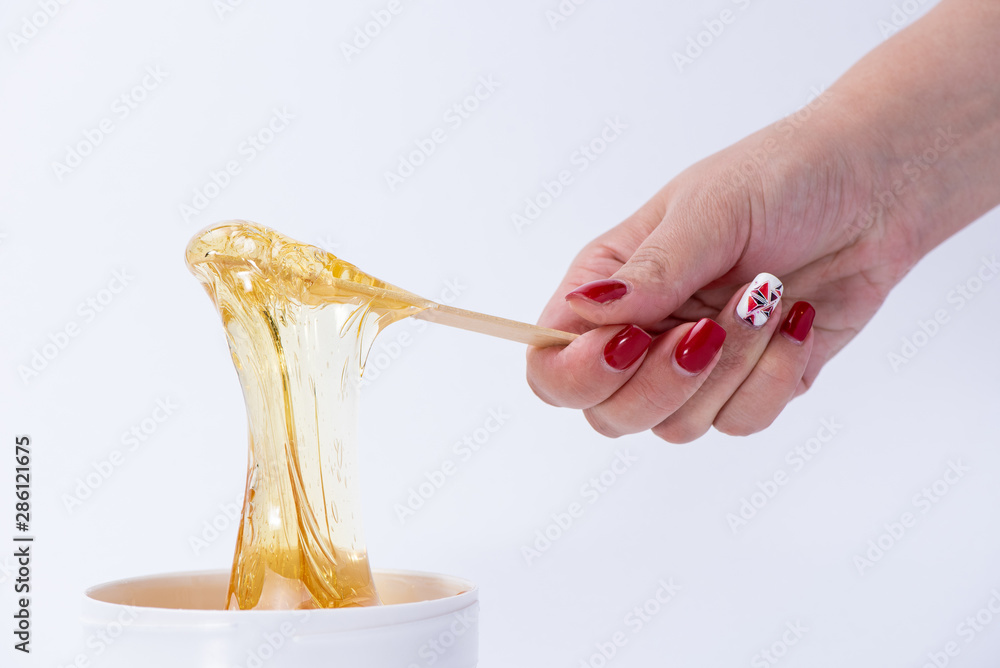 Liquid yellow sugar paste or wax for depilation on a stick close-up on a white background - obrazy, fototapety, plakaty 