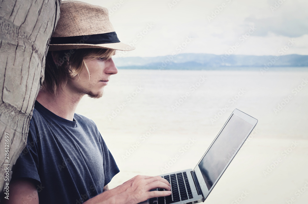 Young man freelancer uses a computer on the shore