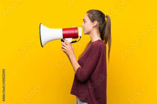 Young woman over isolated yellow background shouting through a megaphone