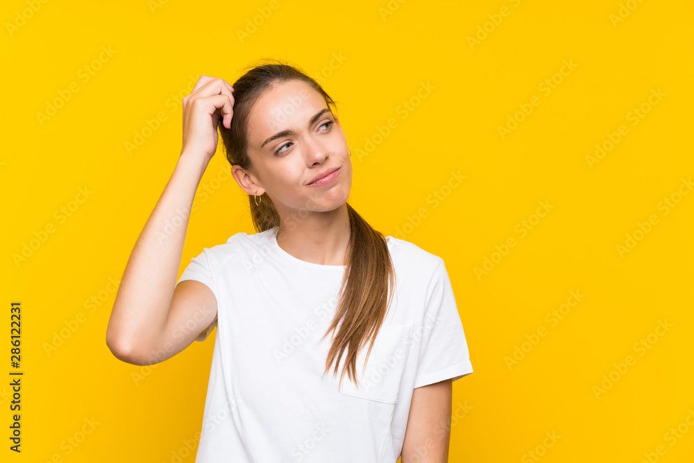 Young woman over isolated yellow background having doubts and with confuse face expression Young woman over isolated yellow background having doubts and with confuse face expression