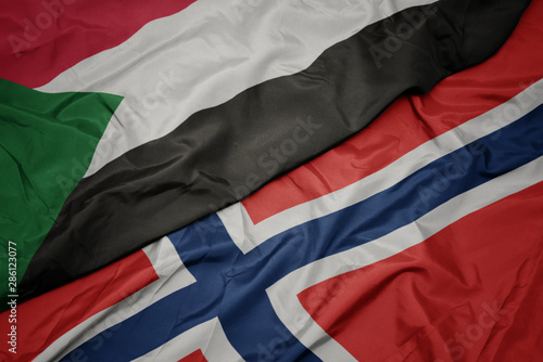waving colorful flag of norway and national flag of sudan.