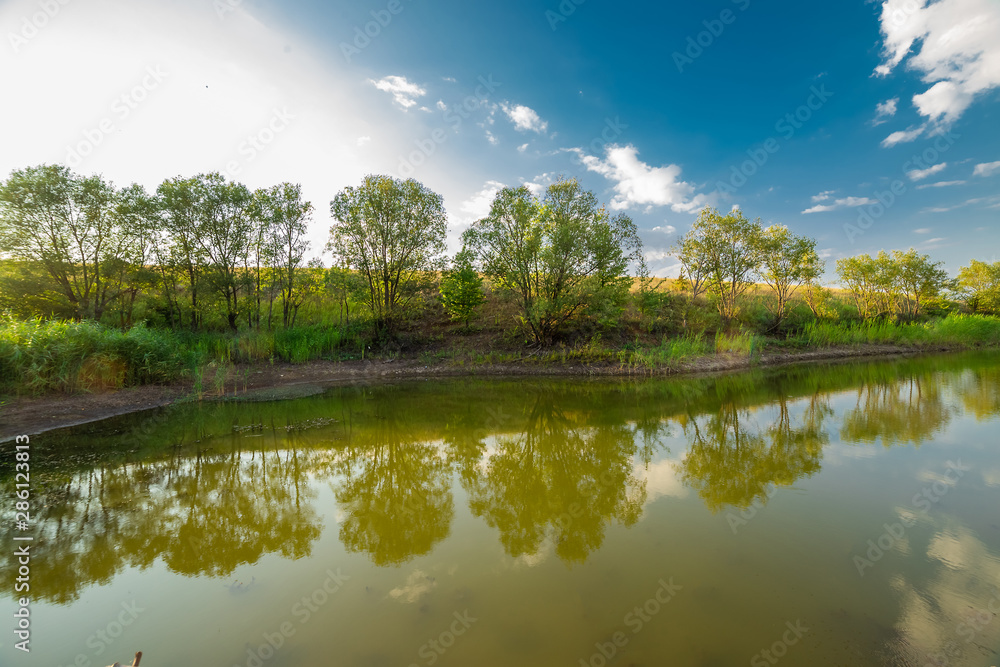 Blue sky, trees and clouds are reflected in the water.