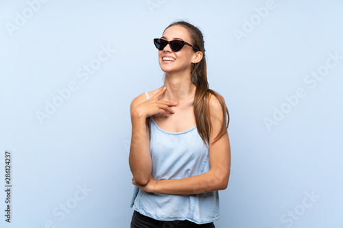 Young woman over isolated blue background with glasses and smiling