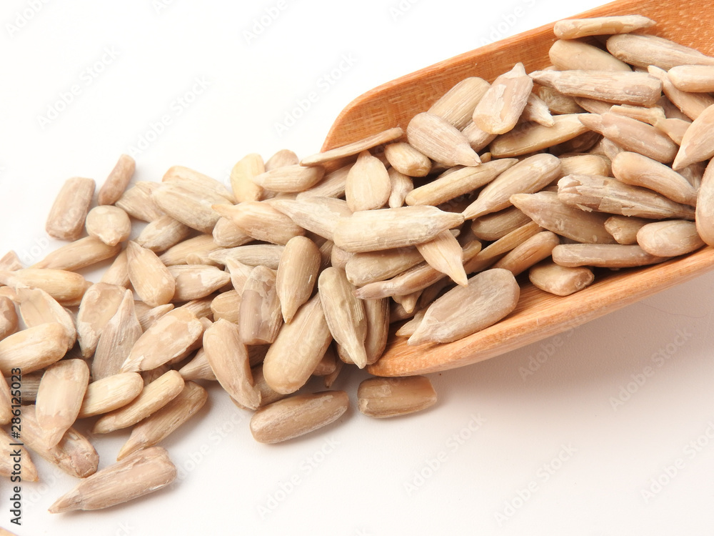 High angle view of natural shelled organic sunflower seeds on wooden spoon isolated on white background. It often eaten as a snack. The seeds contain vitamin E. Food, snack concept. With copy space. High angle view of natural shelled organic sunflower seeds on wooden spoon isolated on white background. It often eaten as a snack. The seeds contain vitamin E. Food, snack concept. With copy space.