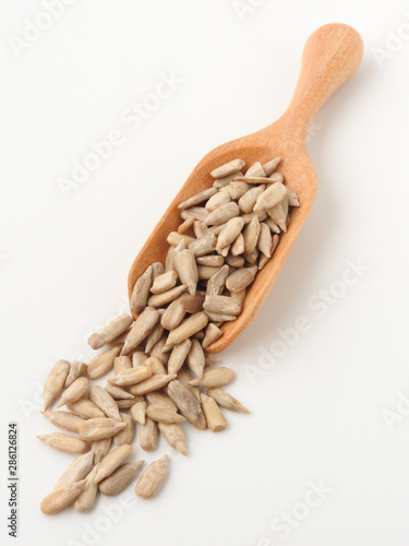 Top view of natural shelled organic sunflower seeds on wooden spoon isolated on white background. It often eaten as a snack.  The seeds contain vitamin E. Food and snack concept.