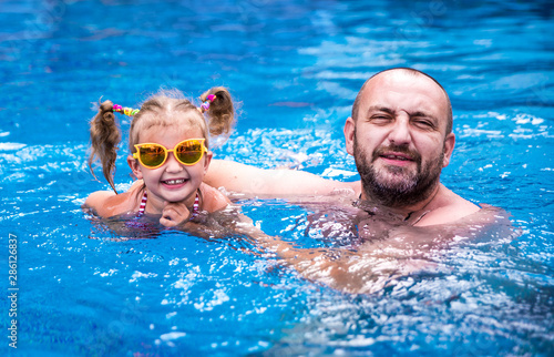 Dad teaches a little daughter to swim in the pool. © seqoya