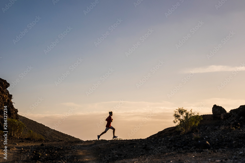 beautiful silhouette of teeenager or man running alone and doing a fit session in mountain with sunset - positive lifestyle - caucasian 20s guy