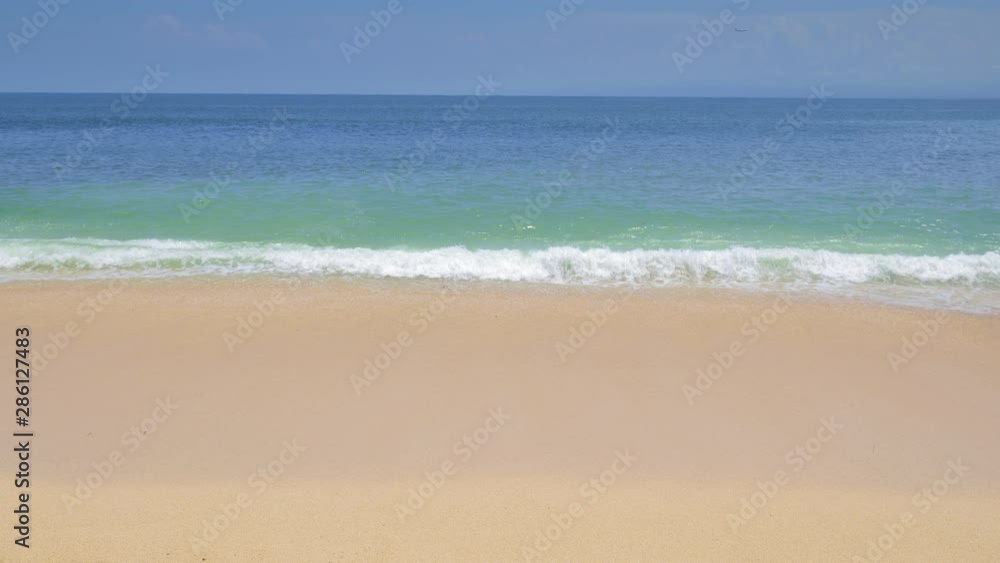 Panoramic view of blue ocean with big warm waves and splashes from sandy beach under clean blue sky and plane landing in background Panoramic view of blue ocean with big warm waves and splashes from sandy beach under clean blue sky and plane landing in background