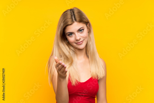 Teenager girl over isolated yellow background handshaking after good deal