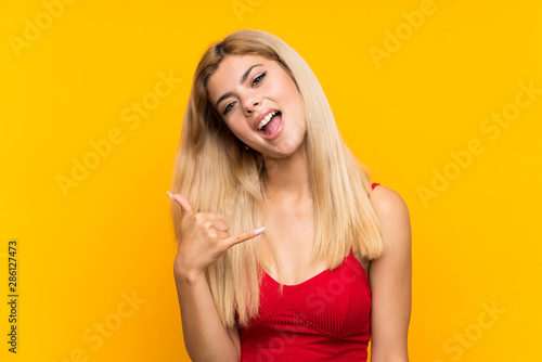 Teenager girl over isolated yellow background making phone gesture